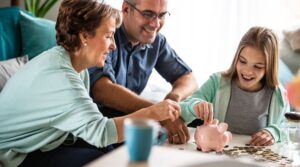 Family teaching children about saving money using a piggy bank at home.