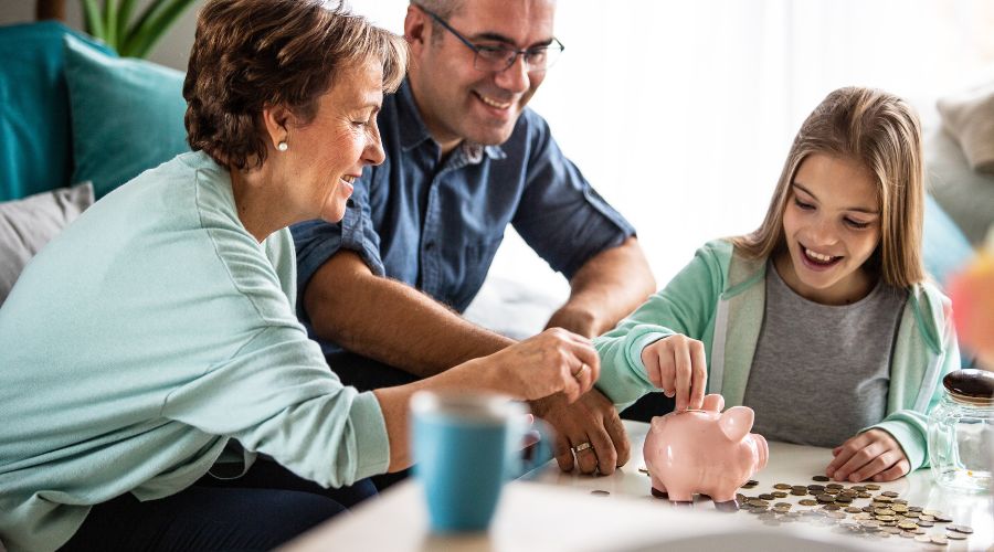 Family teaching children about saving money using a piggy bank at home.