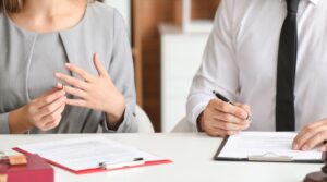 Woman removing her wedding ring while seated beside a professional reviewing documents during a divorce or separation.